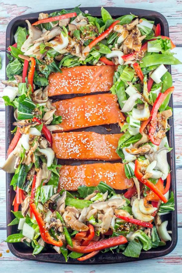 a sheet pan filled with vegetables and raw salmon covered in an asian-inspired sauce