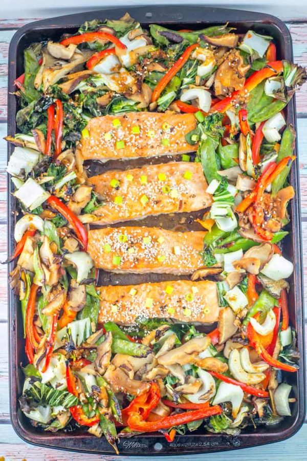 sheet pan full of cooked asian vegetables and four large salmon filets covered in an asian sauce