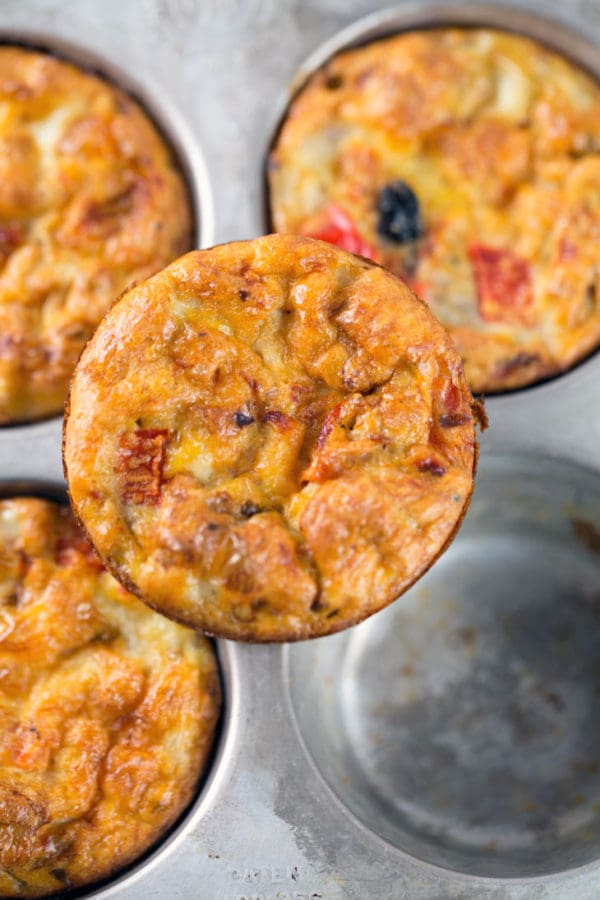 close up view of an egg muffin sitting on a muffin tin showing the flecks of salsa and red peppers