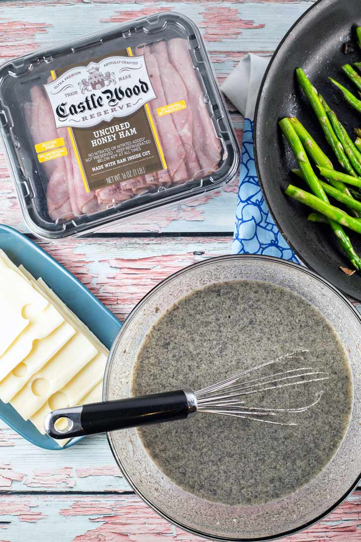 The necessary ingredients for ham asparagus crepe rolls: sliced ham, cheese, asparagus, buckwheat crepe batter.