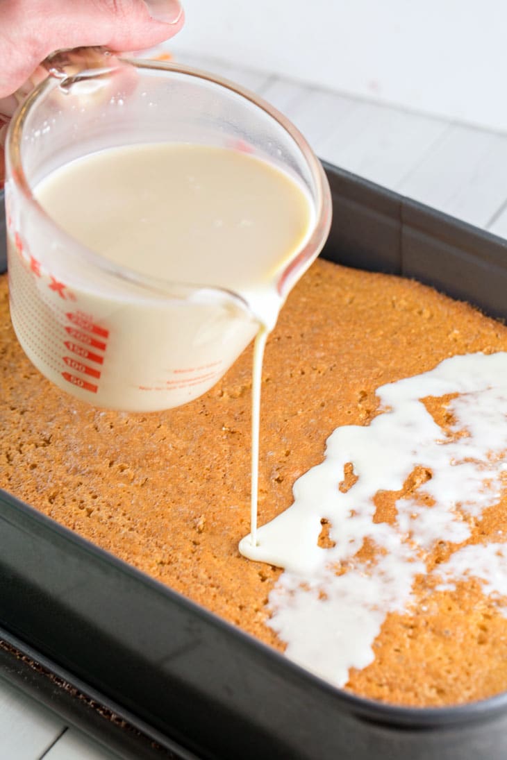 Pouring the three milk glaze over a vanilla sponge tres leches cake.