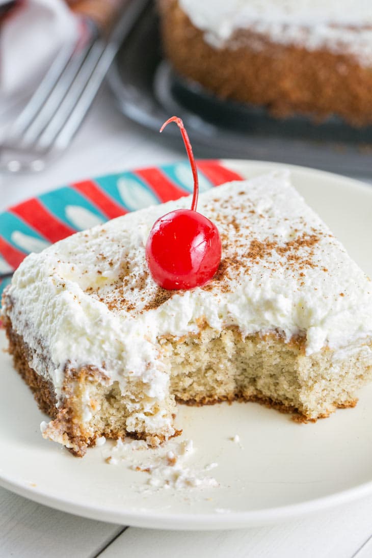 A few bites taken from a slice of Tres Leches Cake with a sprinkle of cinnamon and a cherry.