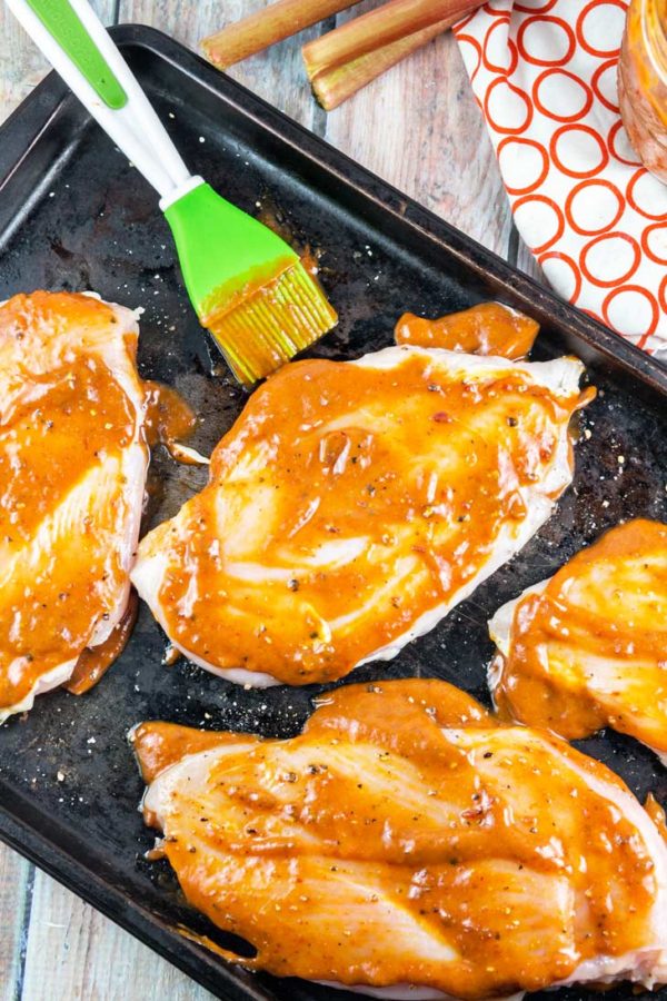 raw chicken breasts on a sheet pan with chipotle rhubarb bbq sauce spread across the top