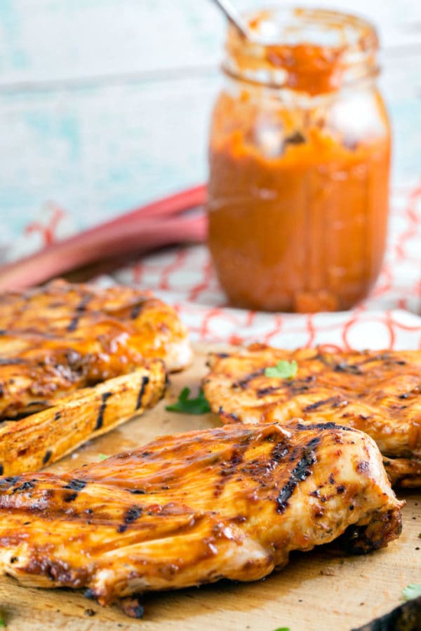 grilled chicken breasts covered in spicy chipotle rhubarb bbq sauce with the jar of sauce in the background