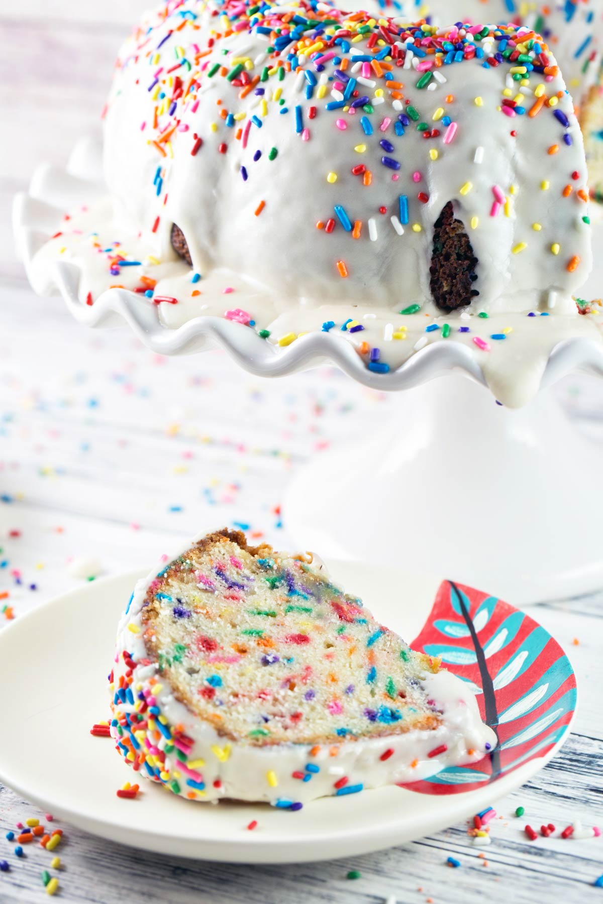 slice of sprinkle-covered cake next to a cake stand.