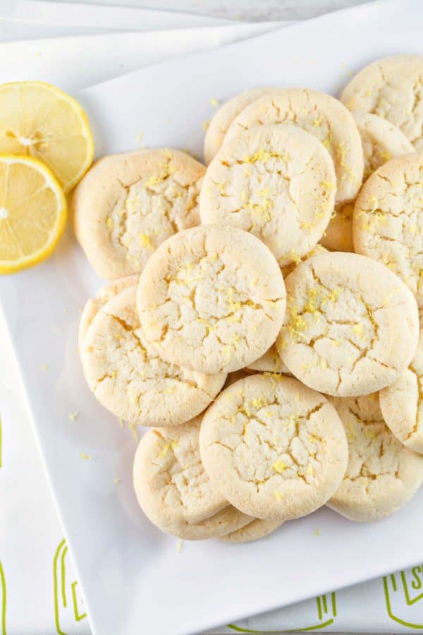 a pile of lemon sugar cookies covered in lemon zest on a white serving plate