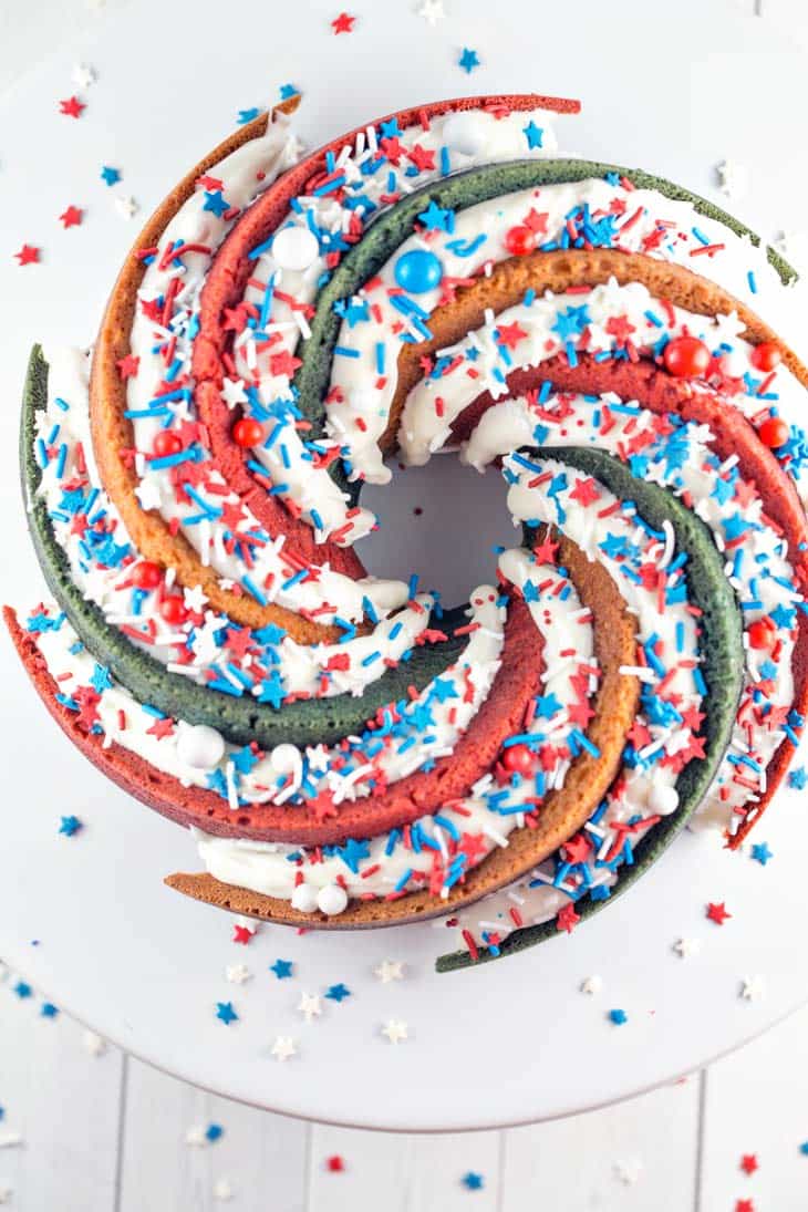 red white and blue spiral bundt cake with white frosting and lots of sprinkles