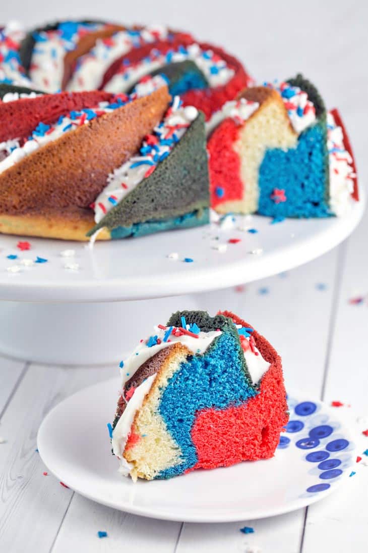 slice of brightly colored red, white, and blue bundt cake next to a cake stand with the rest of the cake