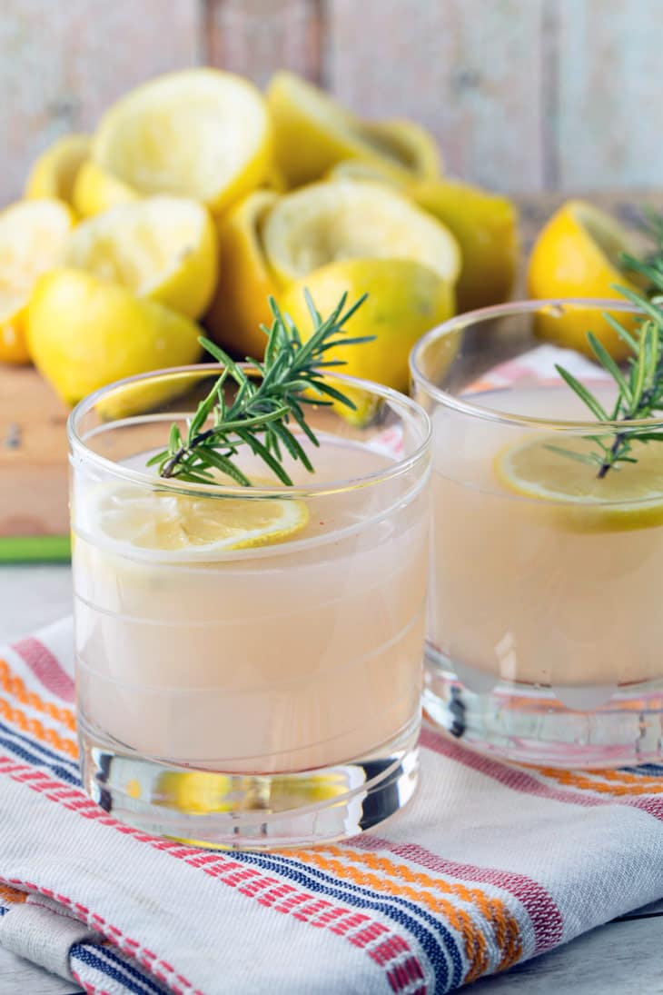 glasses full of rosemary lavender lemonade in front of a pile of squeezed lemon rinds