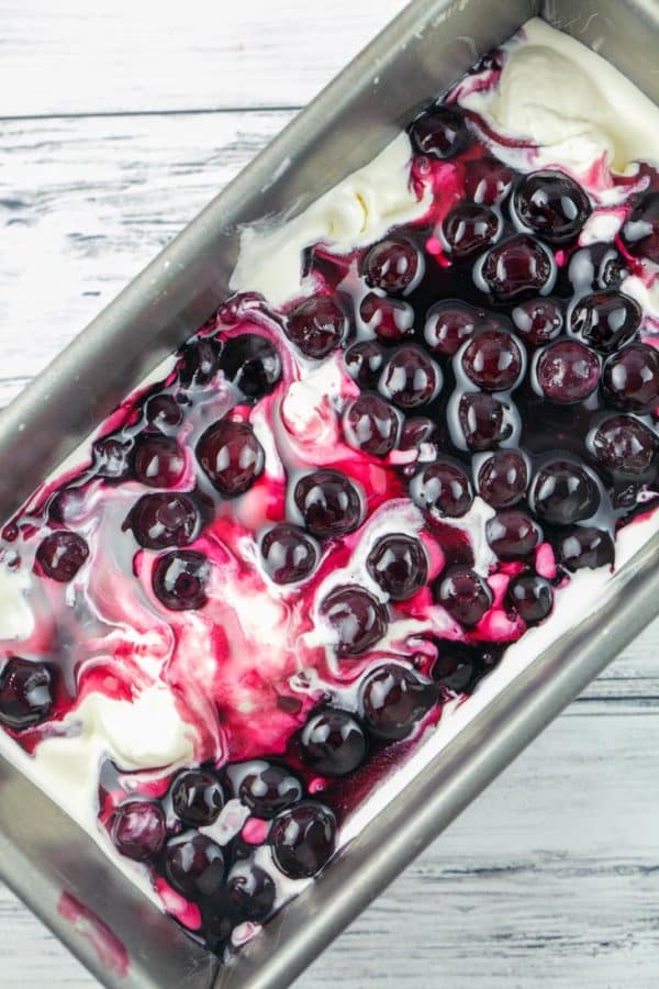 overhead view of sweet cream ice cream with a layer of blueberry pie filling on top to make blueberry pie ice cream