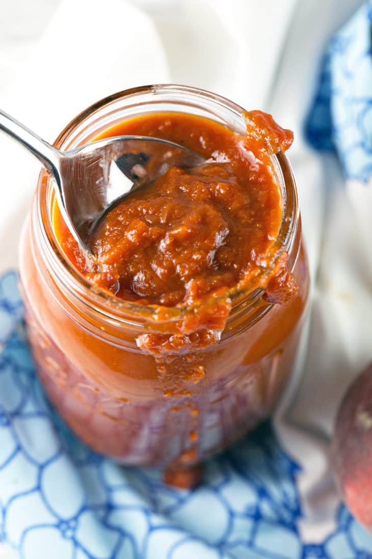 spoon dipping into a glass jar full of peach bbq sauce