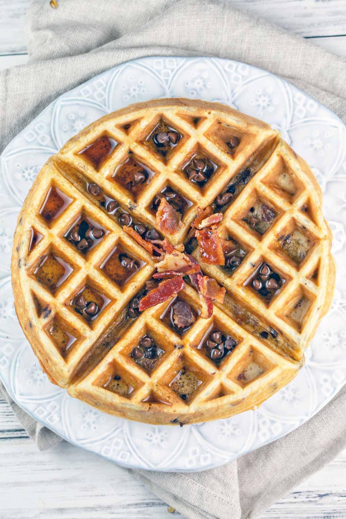 overhead images of a bacon chocolate chip waffle with syrup and extra chocolate chips and bacon sprinkled on top.