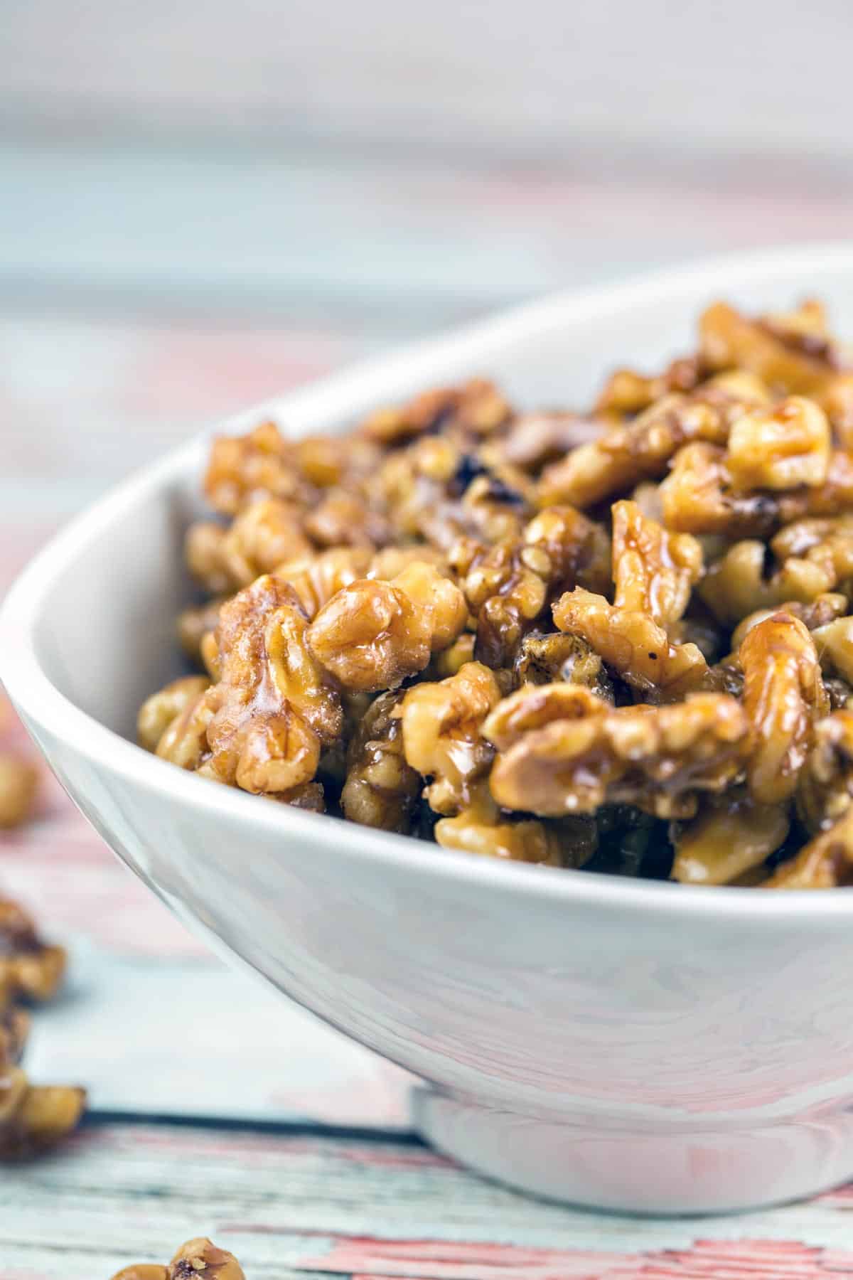 side view of a white bowl filled with maple glazed walnuts.