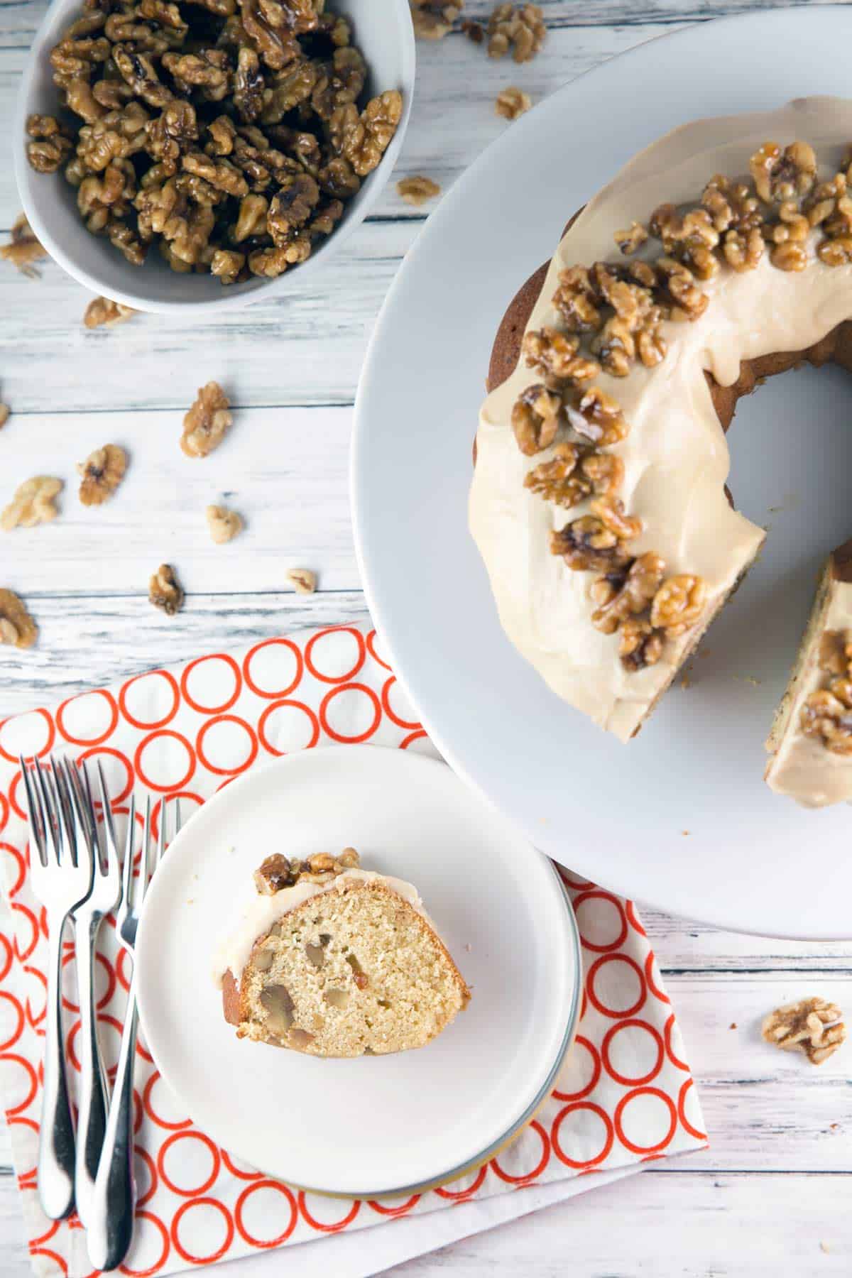 a slice of maple walnut bundt cake on a white dessert plate with the rest of the cake in the background