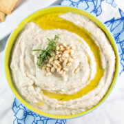 green bowl filled with creamy white bean dip with a swirl of olive oil on top