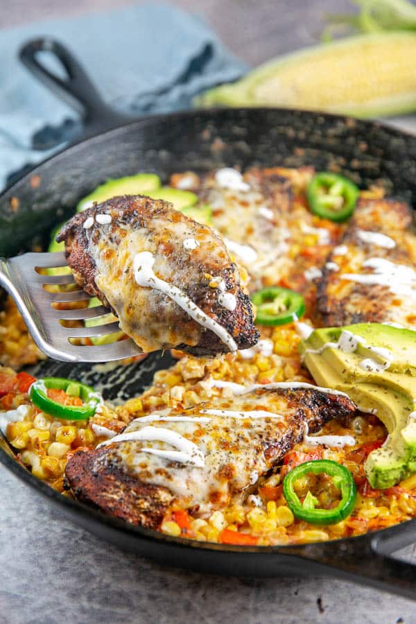 a piece of chicken on a spatula getting lifted out a of a cast iron skillet