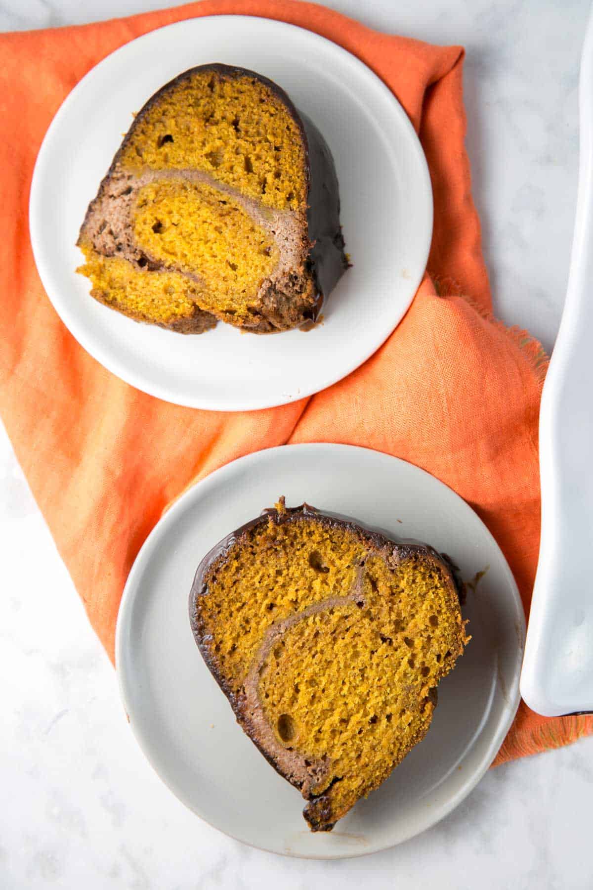 two small plates with slices of pumpkin bundt cake on an orange cloth placemat.