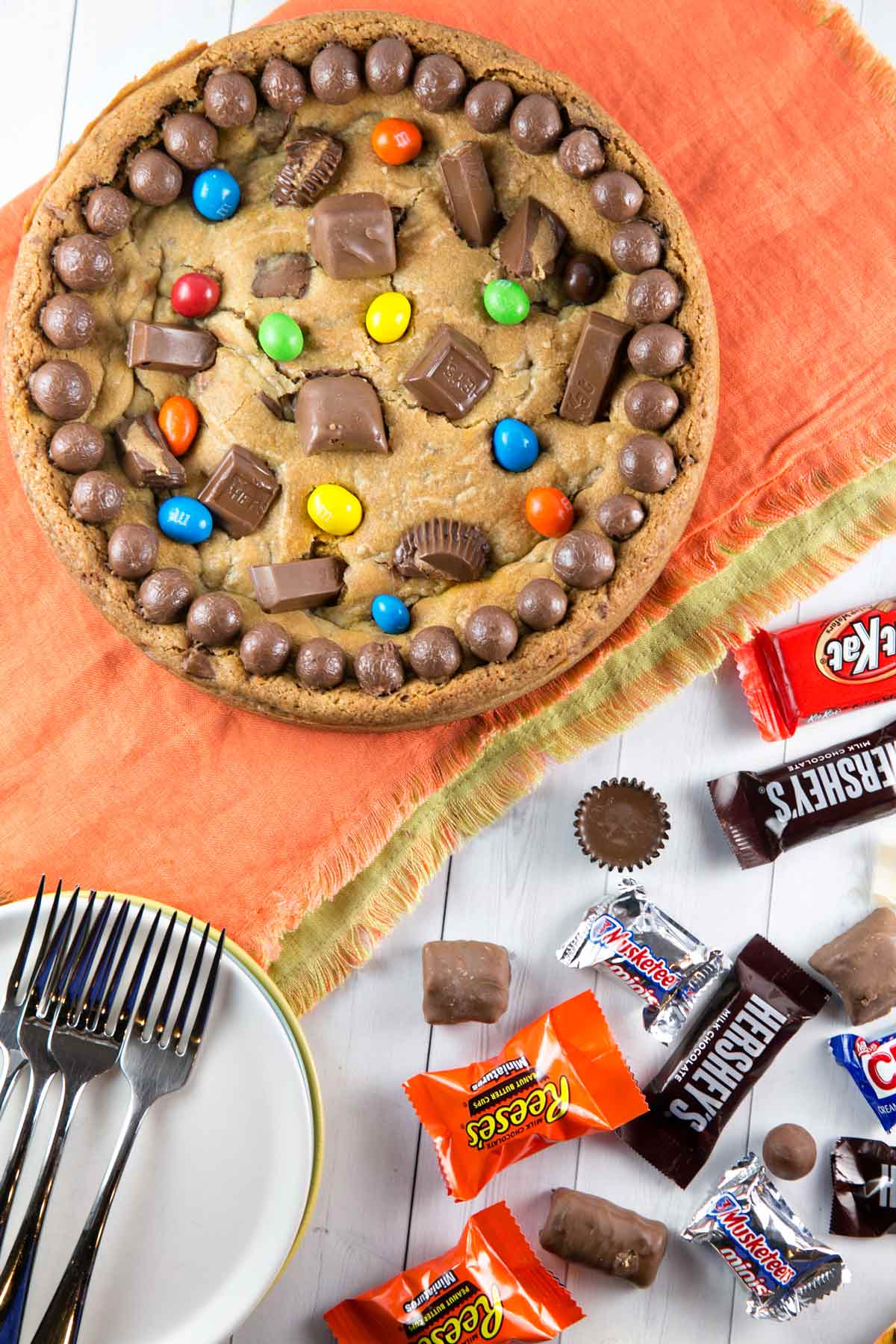 a cookie cake covered in candy on an orange placemat with candy wrappers scattered around.