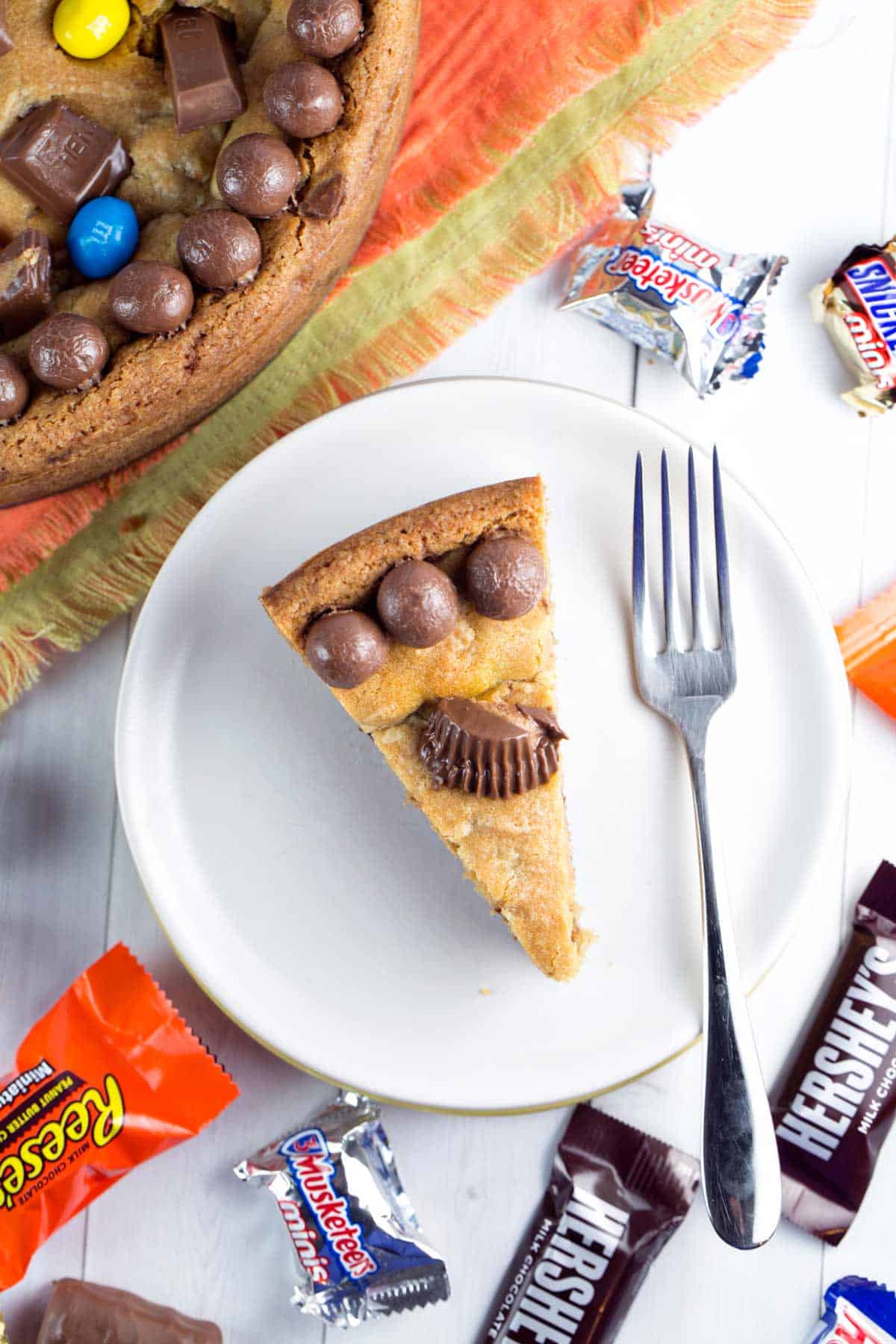 overhead photo of a slice of candy cookie cake with three whoppers and a peanut butter cup
