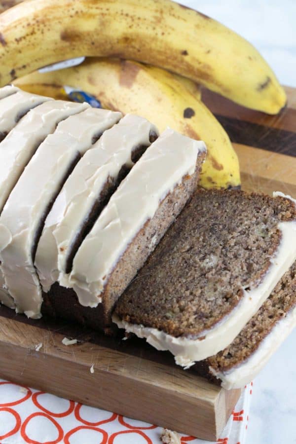 sliced glazed banana bread on a cutting board next to brown spotted bananas