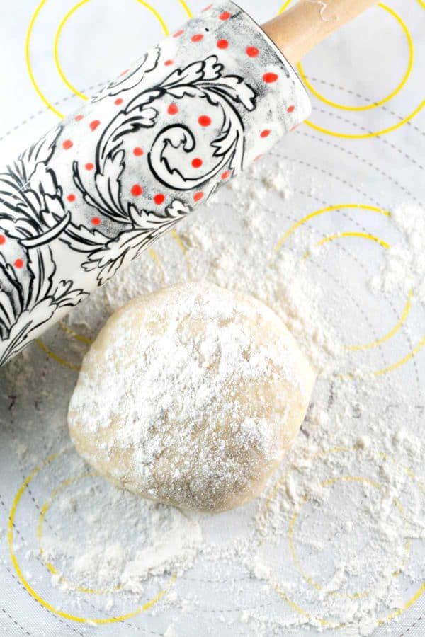 round ball of pie crust dough dusted with flour next to a decorative rolling pin
