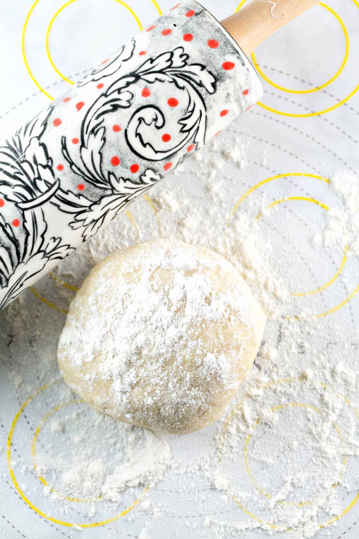 round ball of pie crust dough dusted with flour next to a decorative rolling pin.