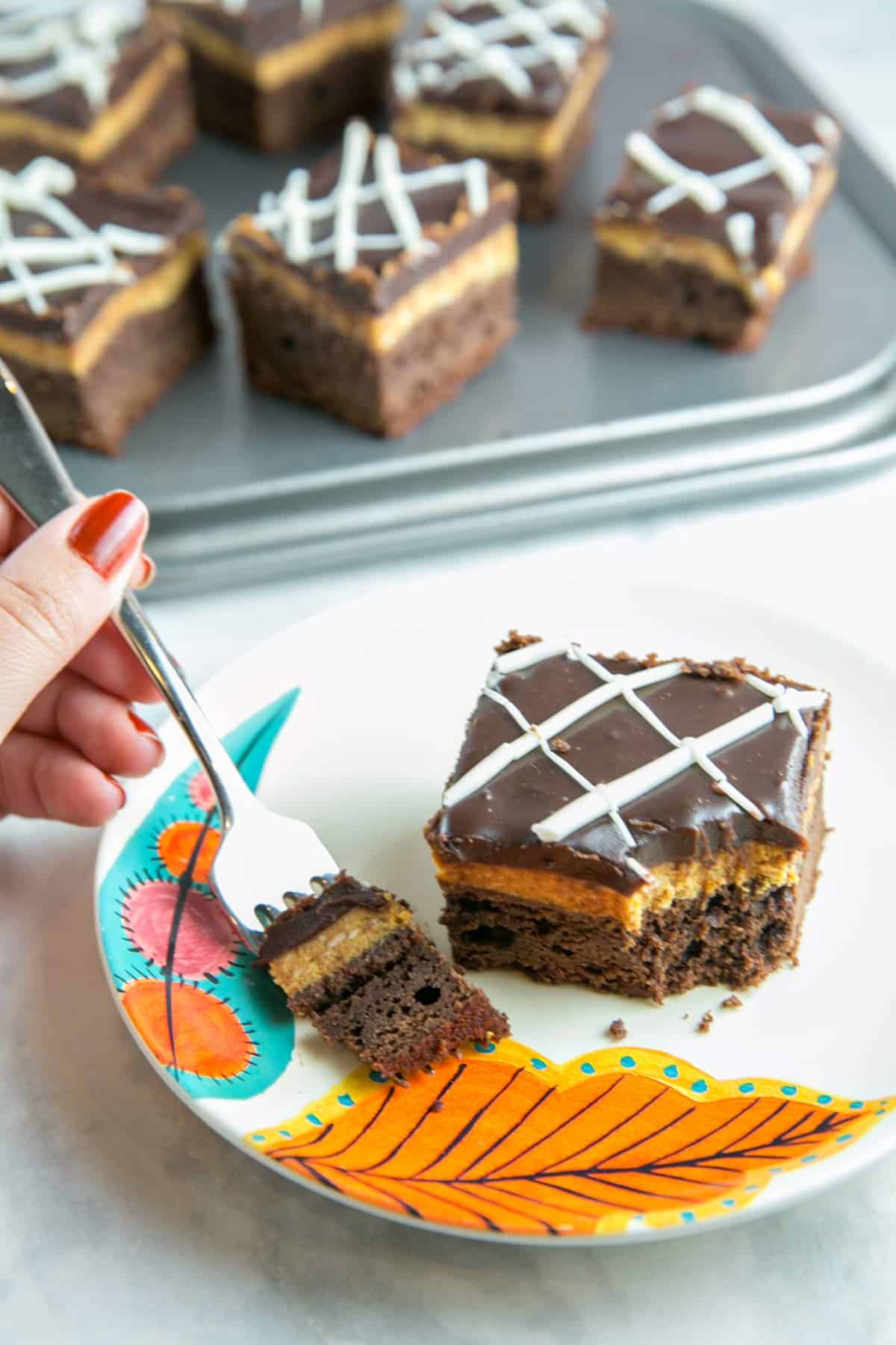 pumpkin cheesecake brownie on a plate with a hand holding a fork.