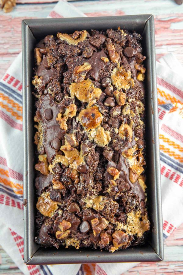 loaf of rocky road banana bread in the loaf pan on an orange pink and white dish towel