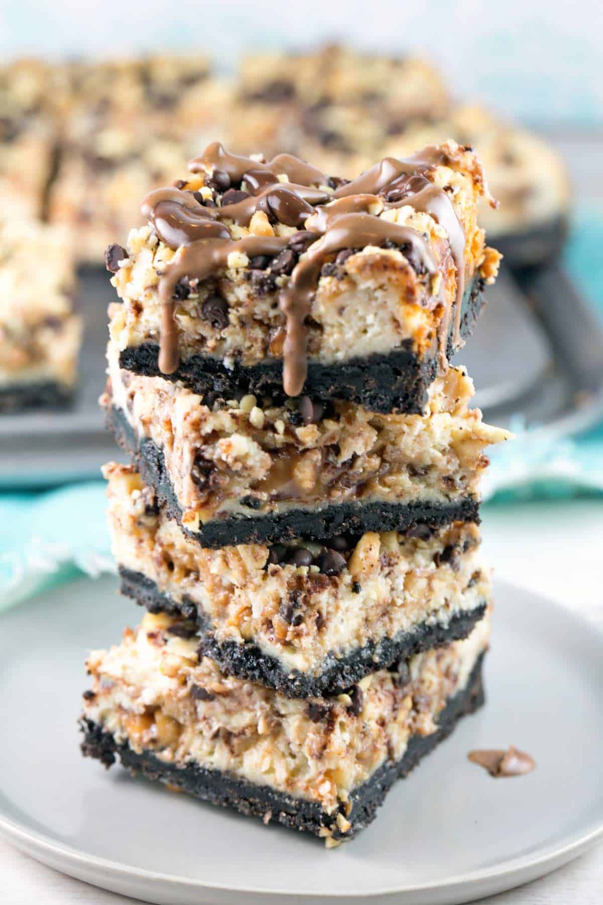 a stack of four snickers cheesecake bars on a gray plate.