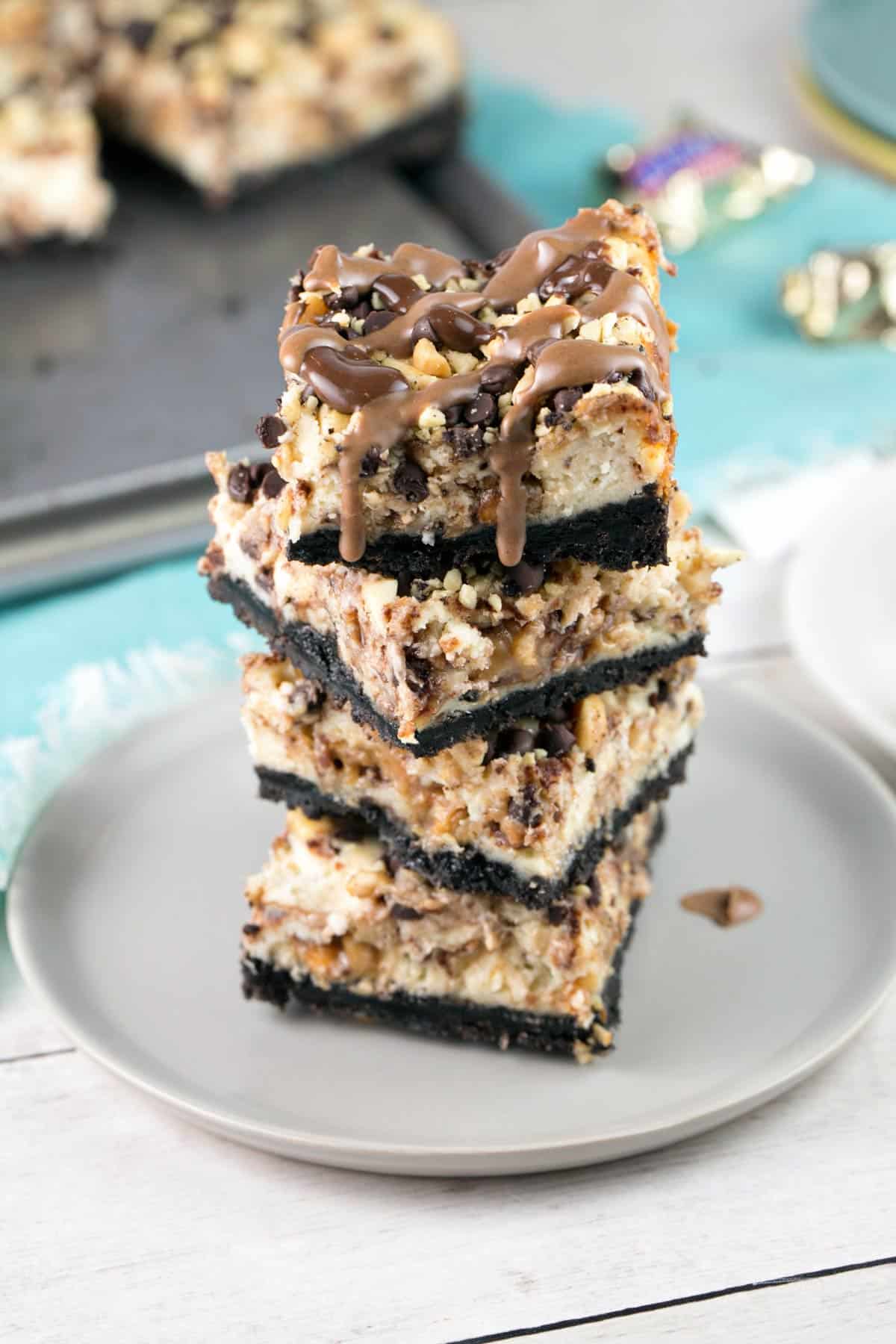 a stack of snickers cheesecake bars with oreo crust with chocolate drizzles.