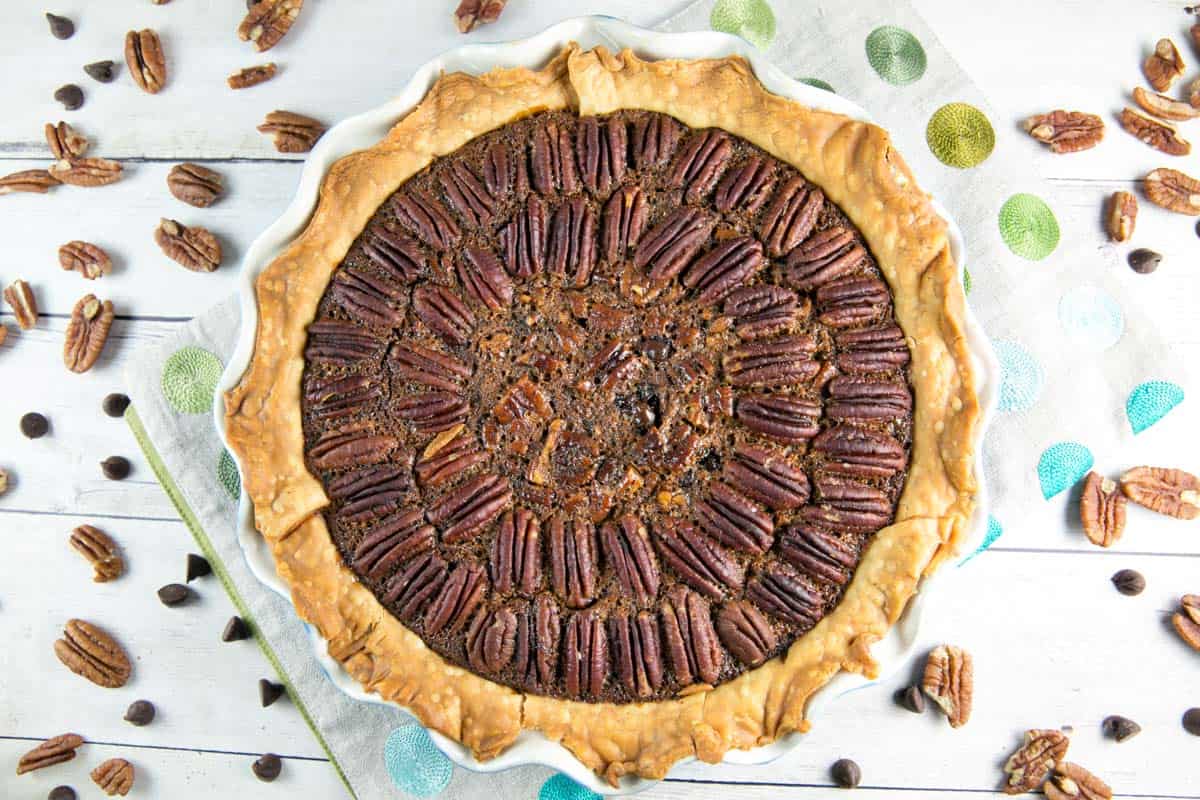 overhead view of a baked chocolate bourbon pecan pie with pecans scattered in the background.