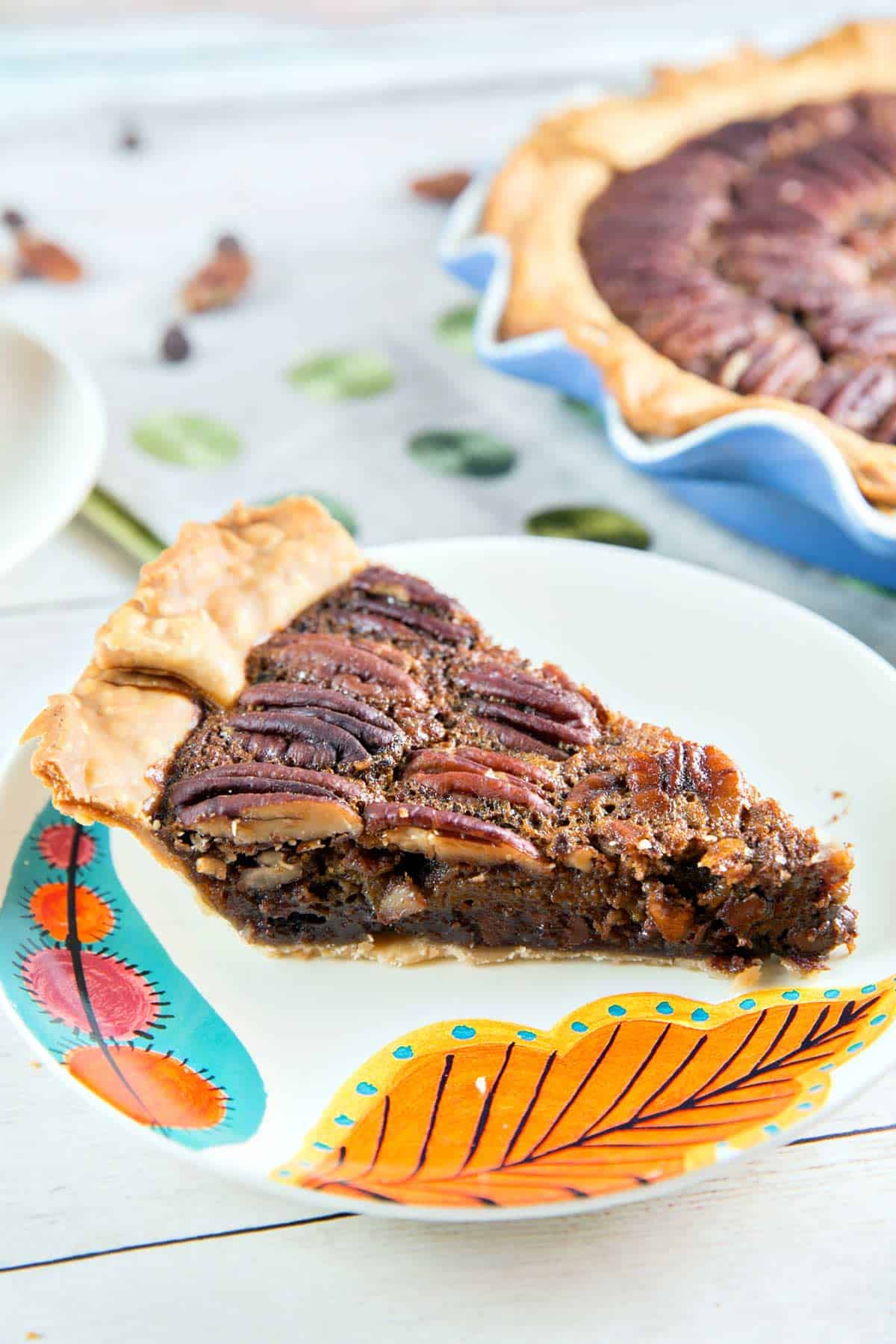 side view of a slice of chocolate bourbon pecan pie on an orange leaf plate
