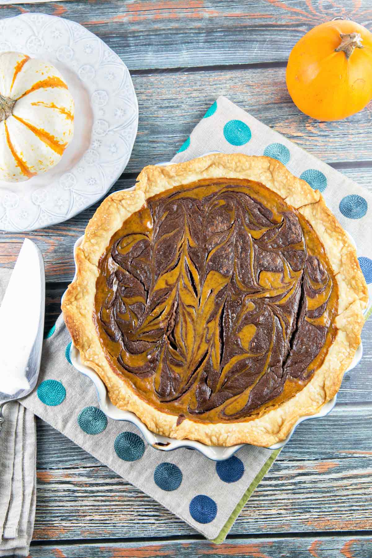 baked pie crust with a nutella swirled pumpkin pie on a placemat with blue dots next to small decorative pumpkins.