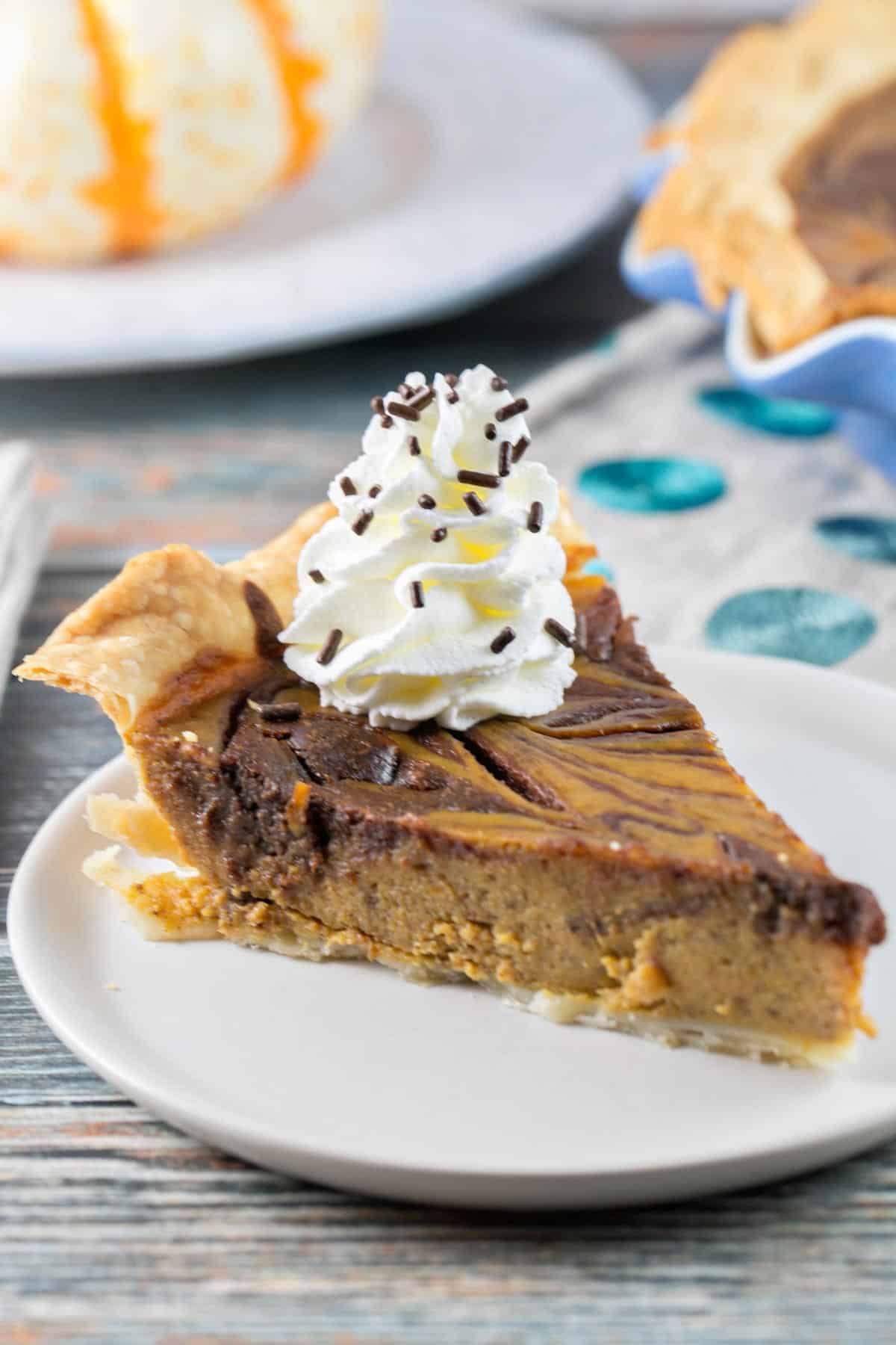 side view of a slice of nutella swirled pumpkin pie with whipped cream and chocolate sprinkles on top.