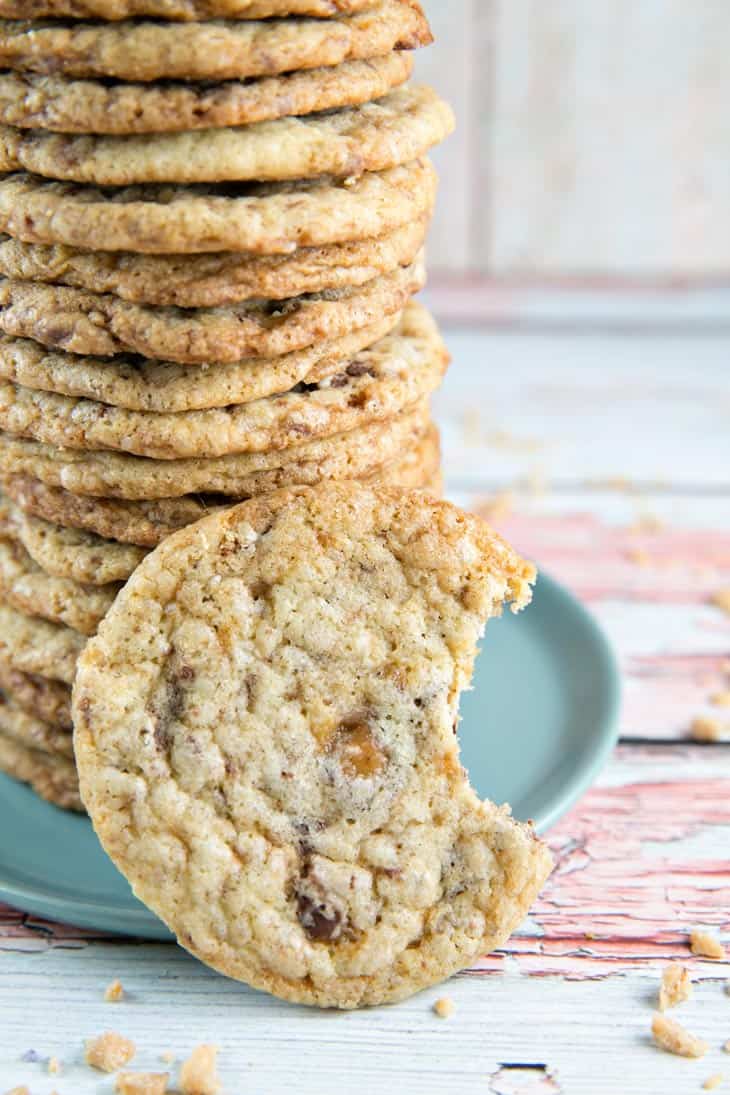 tall stack of toffee crunch cookies with a cookie with a bite taken out of it in front.