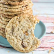 vertical stock of toffee crunch cookies with one cookie in front with a bite taken out of it.