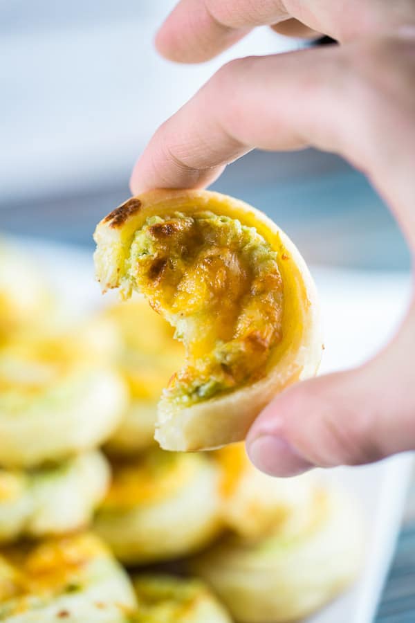 hand holding a puff pastry appetizer with one bite removed.