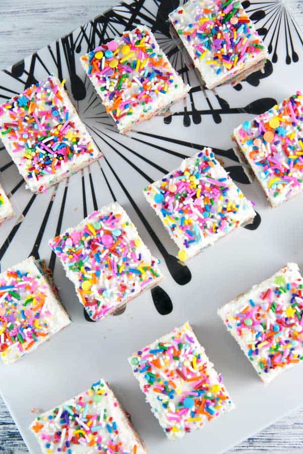 frosted sugar cookie bars covered in sprinkles on a decorative serving plate.