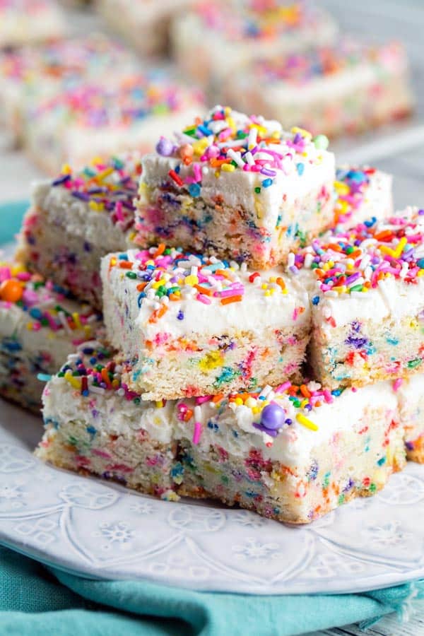 stacked pile of sugar cookie bars covered with a thick layer of frosting and lots of sprinkles.