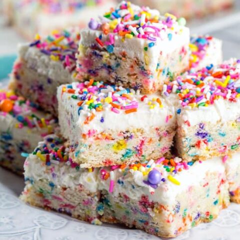 pile of funfetti cookie bars with a thick layer of frosting and lots of sprinkles.