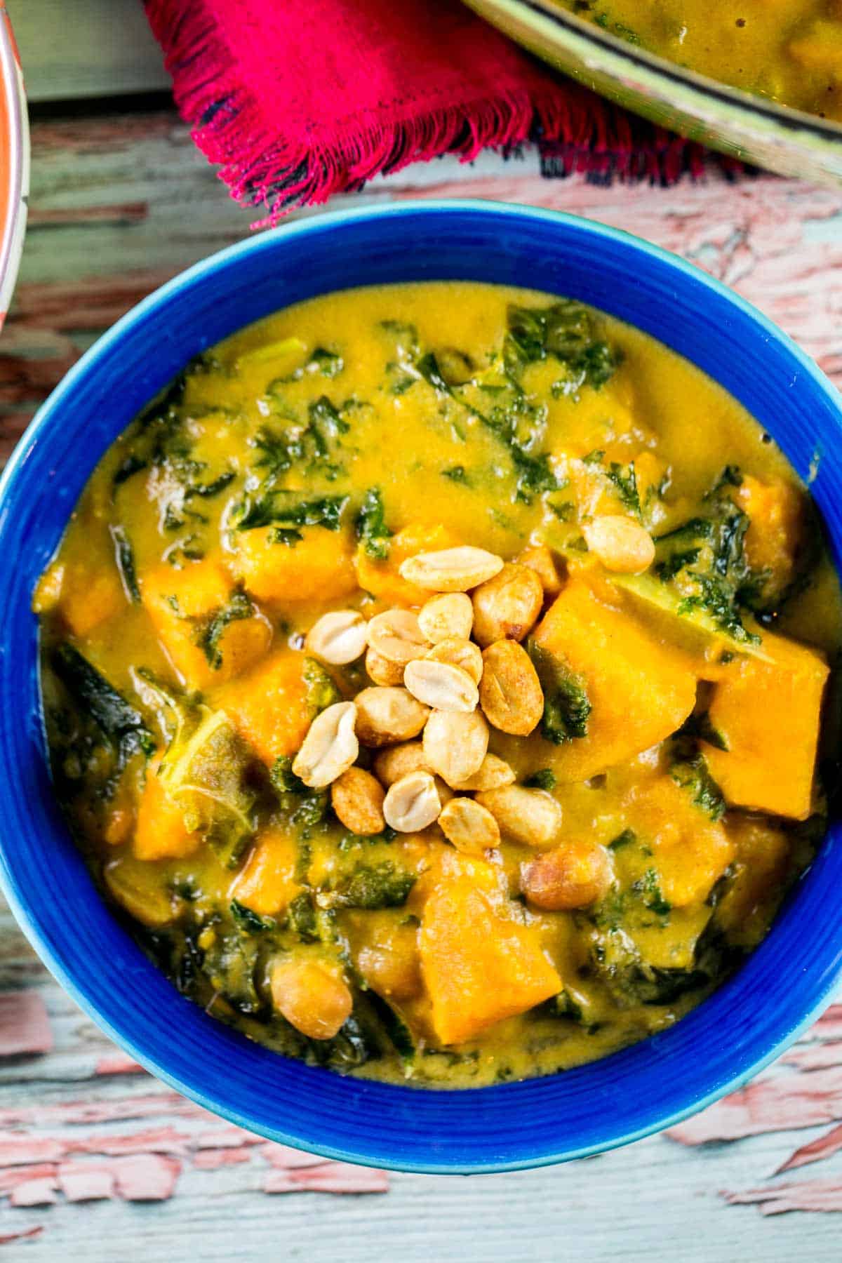 close up view of a bowl of sweet potato soup with kale and peanuts sprinkled on top.