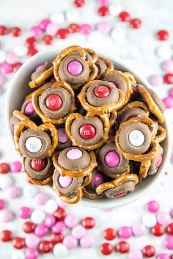 M&M Pretzel Kisses: a pretzel, a Hershey kiss, and a fun colored M&M -- so easy, but the bite-sized sweet and salty combination is irresistible. Match M&M colors to holidays for a fun school treat! #dessert #valentines