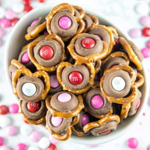 M&M Pretzel Kisses: a pretzel, a Hershey kiss, and a fun colored M&M -- so easy, but the bite-sized sweet and salty combination is irresistible. Match M&M colors to holidays for a fun school treat! #dessert #valentines