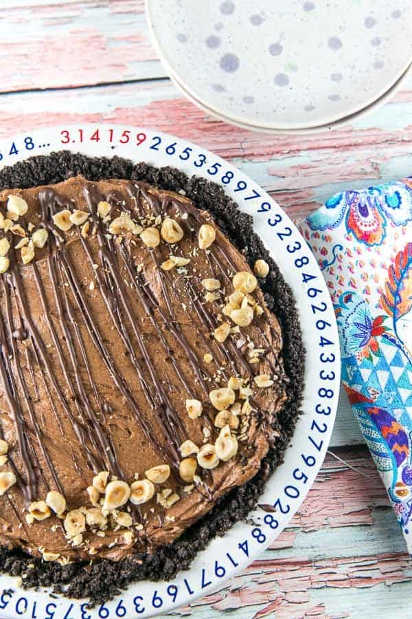 a no bake nutella pie in an oreo crust topped with drizzled of chocolate and chopped hazelnuts
