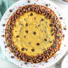 chocolate chip cookie cake decorated with sprinkles on a white cake stand.