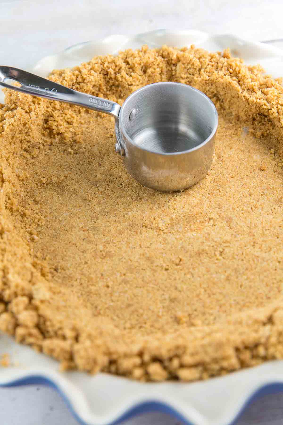 using a measuring cup to press graham cracker crumbs into a pie plate