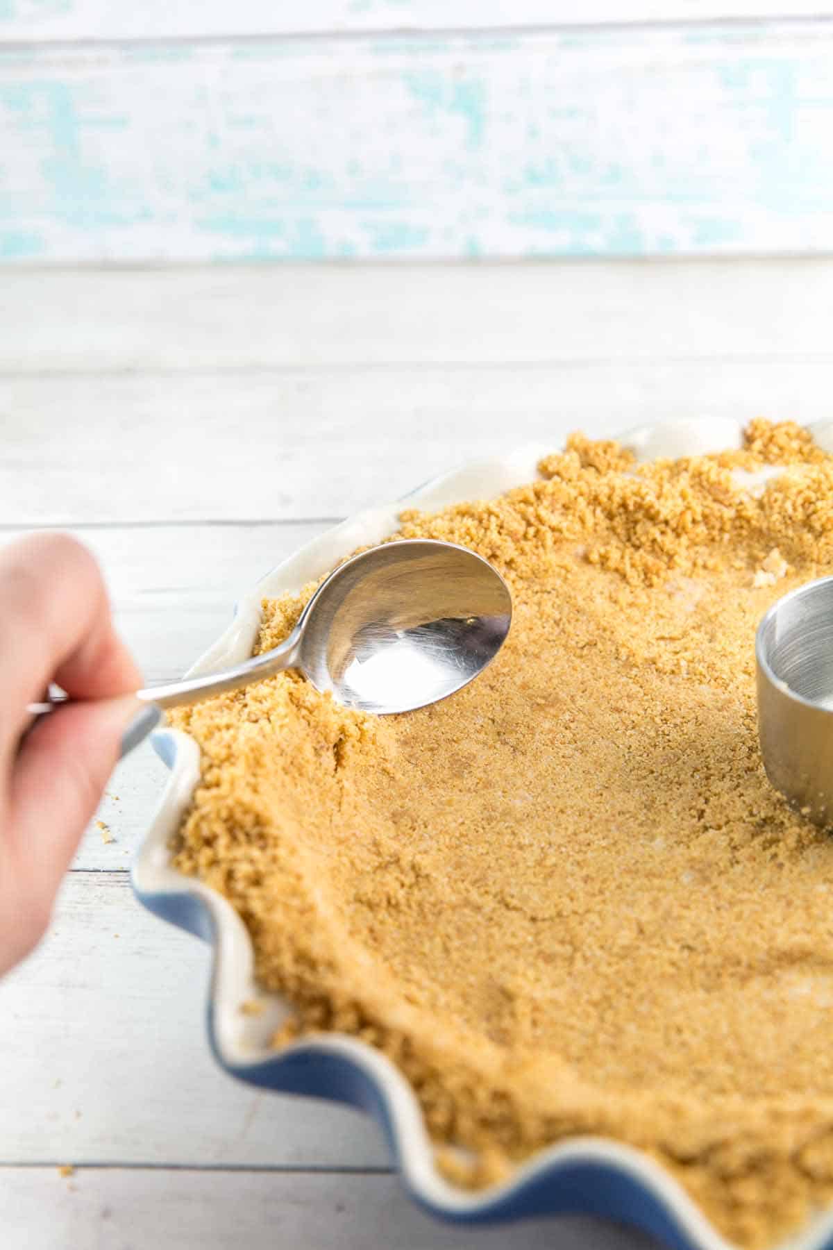 using a spoon to press crumbs up the side of a pie dish