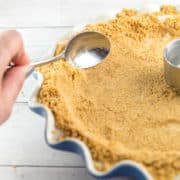 a spoon pressing graham cracker crumbs up the sides of a pie dish