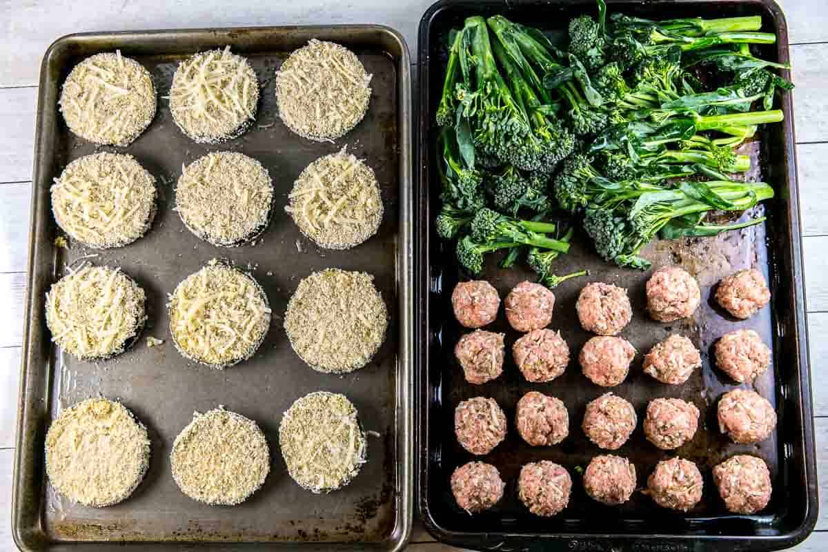 two sheet pans with unbaked eggplant parmesan, turkey meatballs, and broccolini.