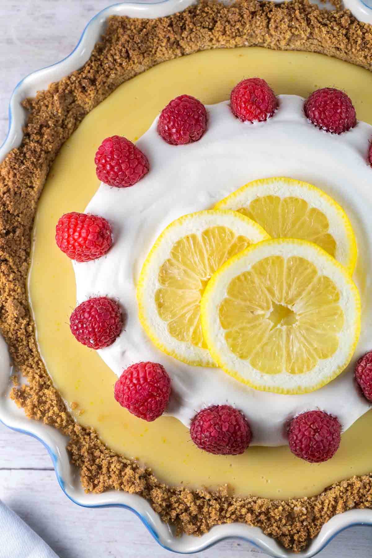 overhead view of a lemon pie covered with whipped cream, raspberries, and lemon slices